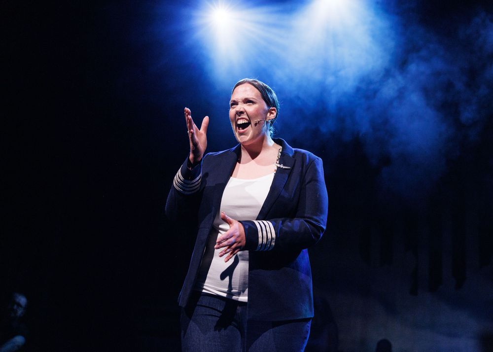 A woman in a navy blazer performs passionately on a smoky, blue-lit stage.