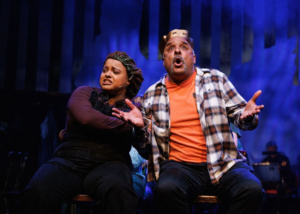 Two performers sing expressively on stage under blue lights during a theatrical production.