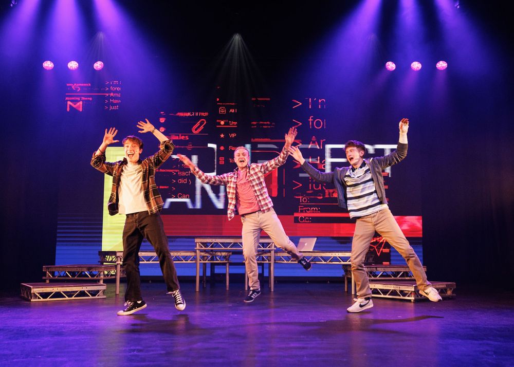 Three performers dancing energetically on a colorful stage with bright lighting and digital backdrop.