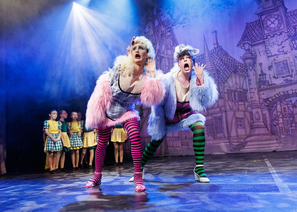 Performers in colorful costumes dance across a stage with dramatic blue lighting and a castle backdrop.