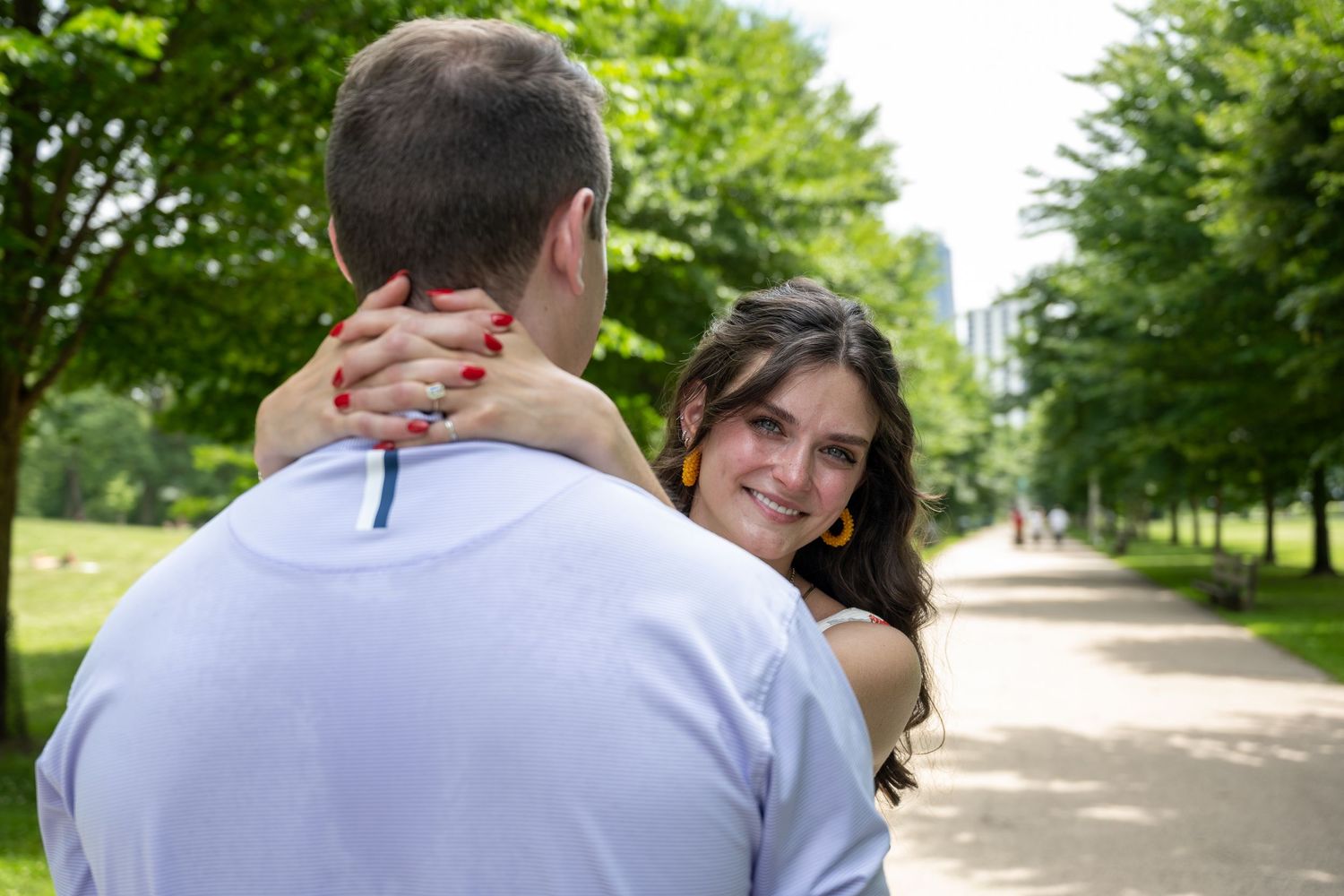 A couple shares a tender moment on a tree-lined path in a summer park.