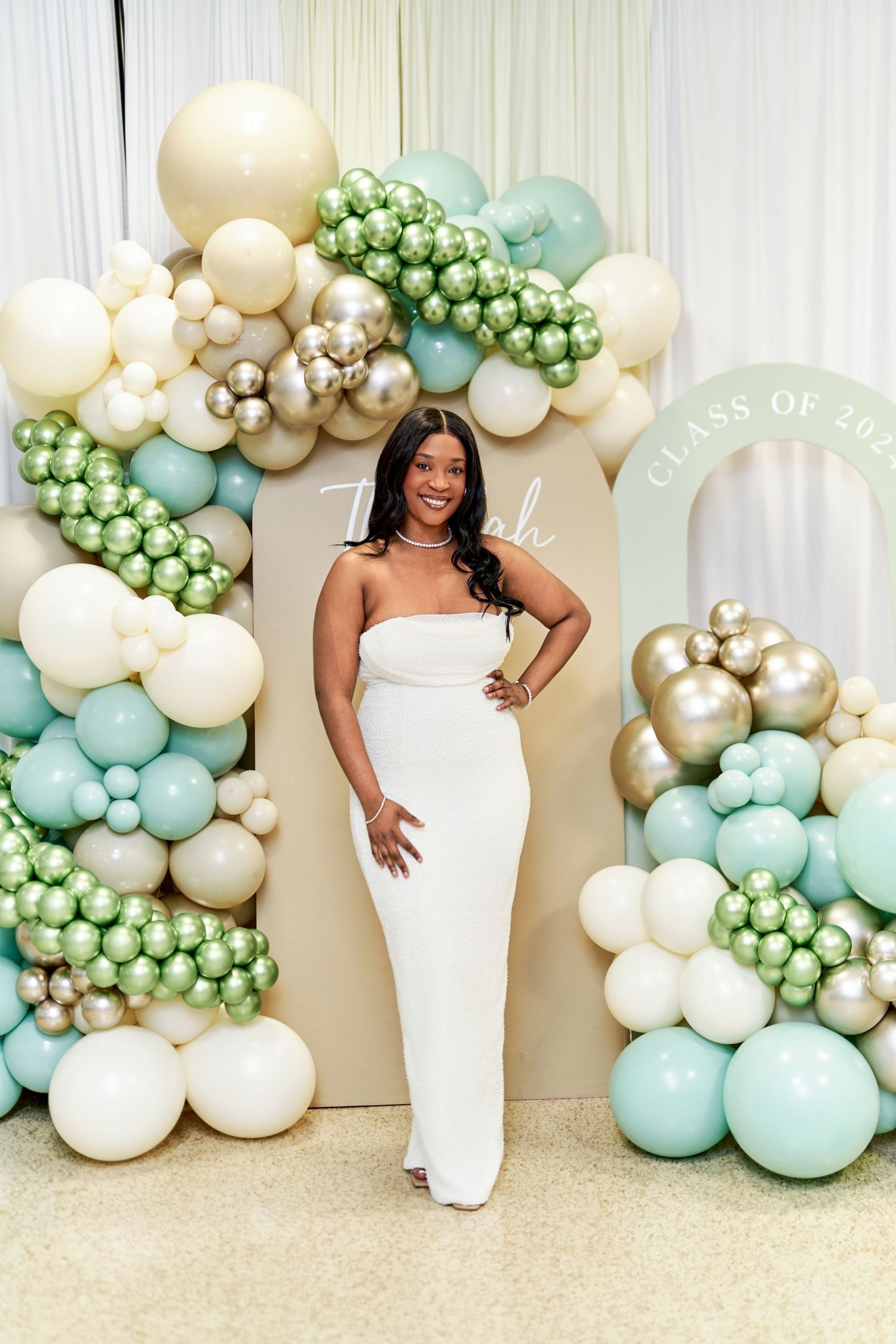 Elegant event setup featuring a luxurious balloon display and a well-dressed woman posing in front of a decorative floral arch