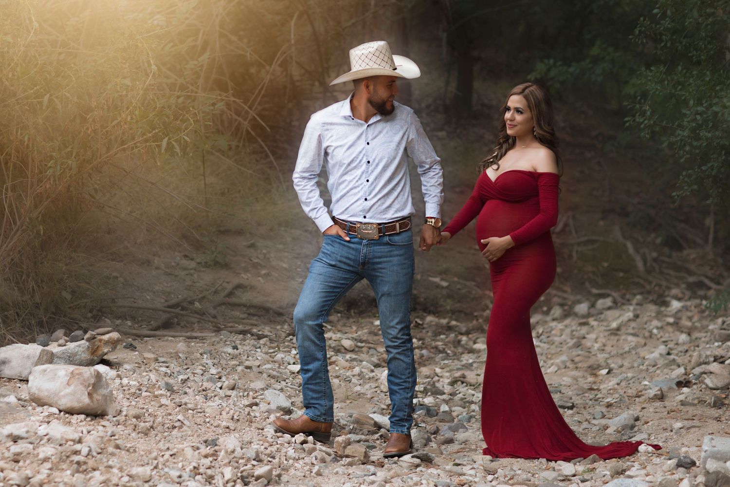 Rustic maternity portrait of couple in western attire against a desert backdrop.