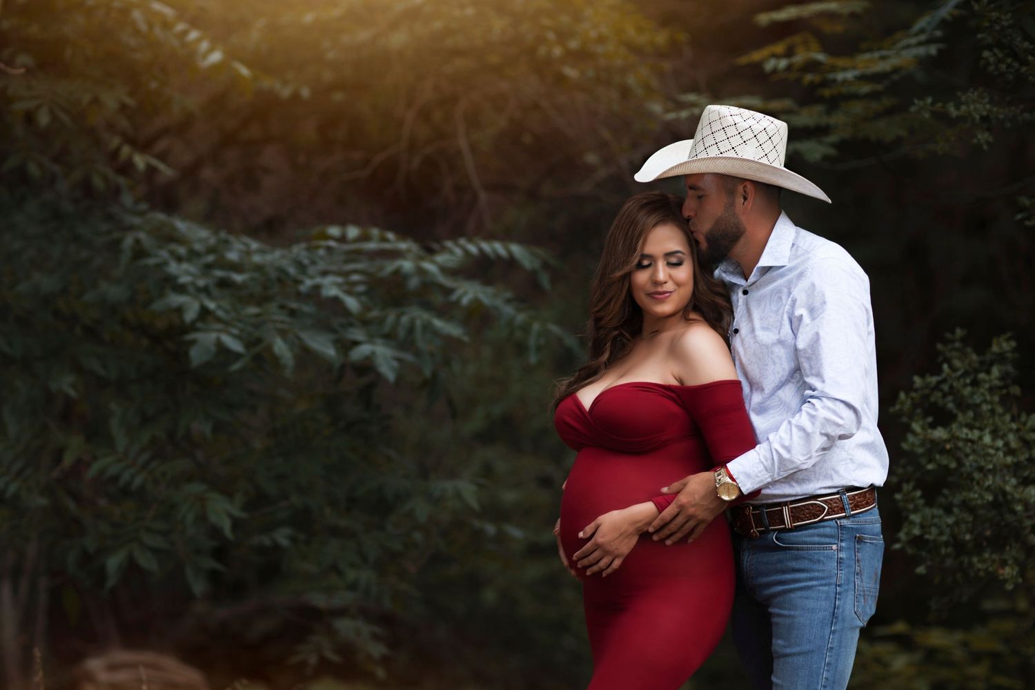 Intimate outdoor maternity portrait showing couple embracing against forest backdrop.