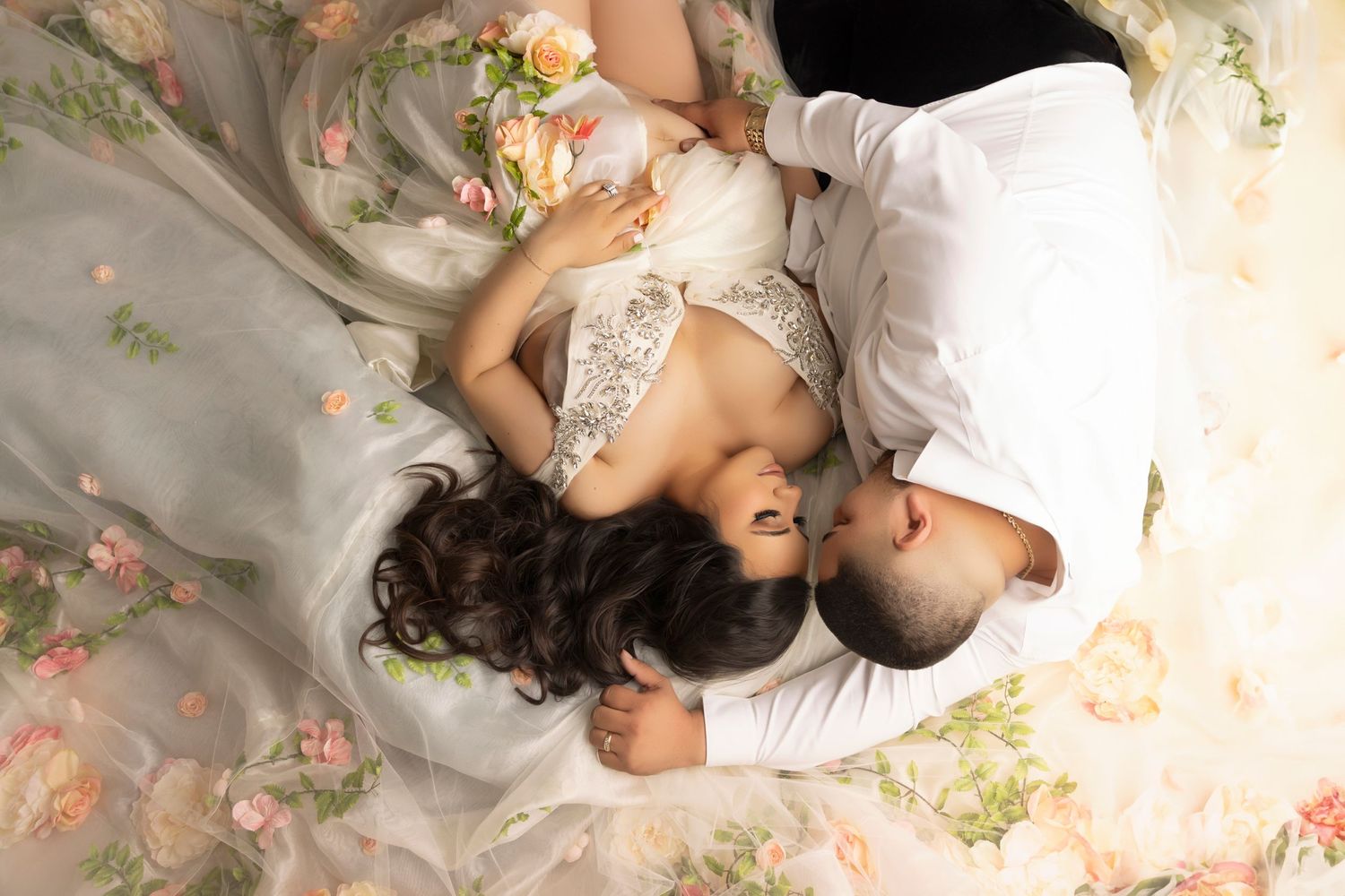 Romantic maternity photo of couple in white with floral dress details.
