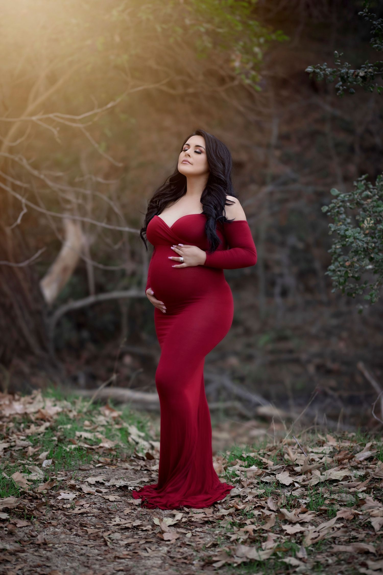 Serene maternity portrait showing an expectant mother in a fitted red dress among fallen leaves.