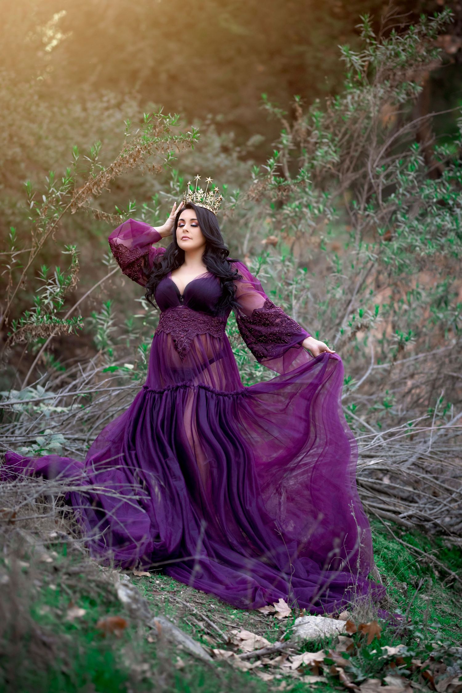 Dramatic outdoor maternity portrait featuring a flowing purple gown in a natural forest setting.