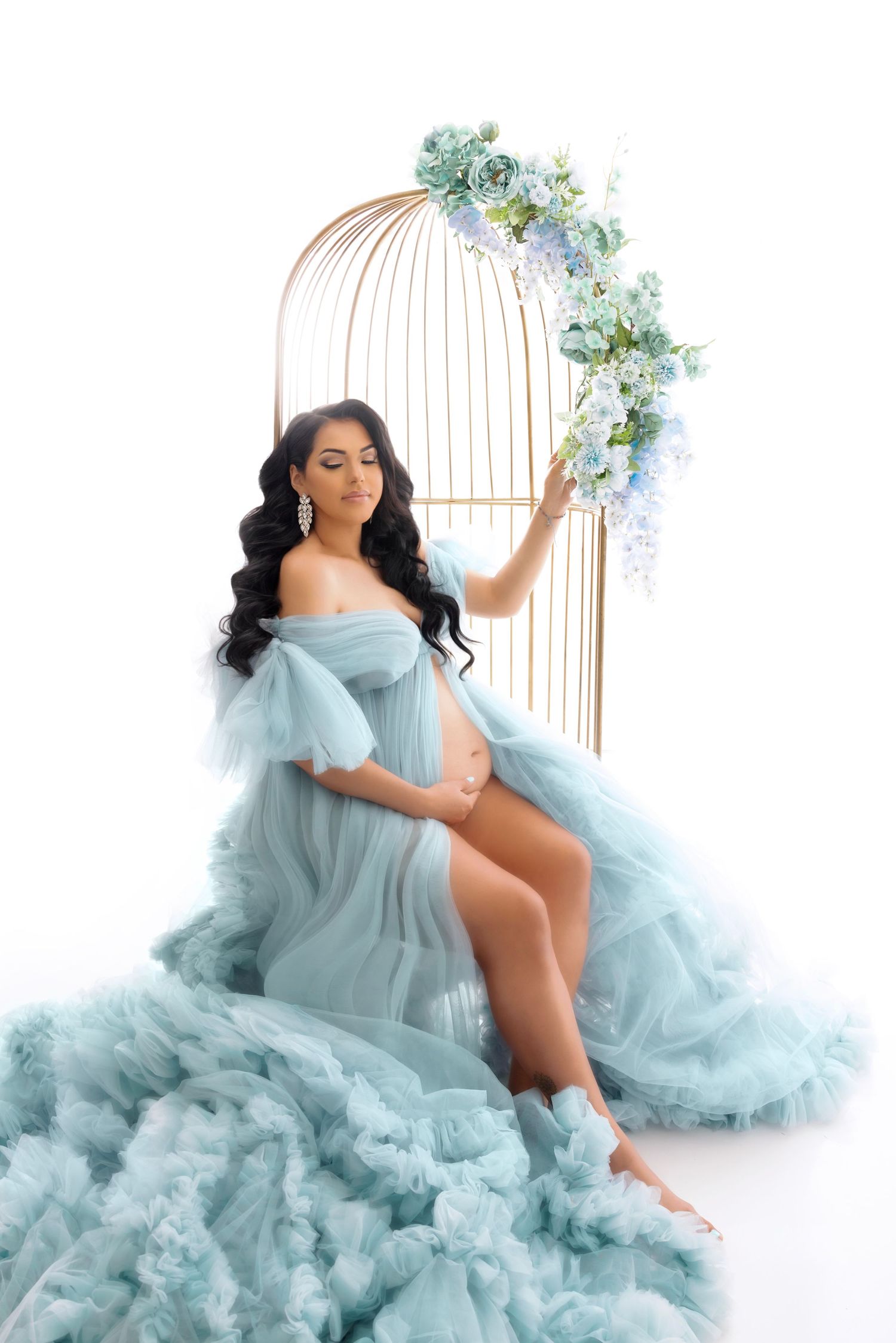 Ethereal maternity photo featuring a flowing blue gown and decorative arch with light blue flowers.