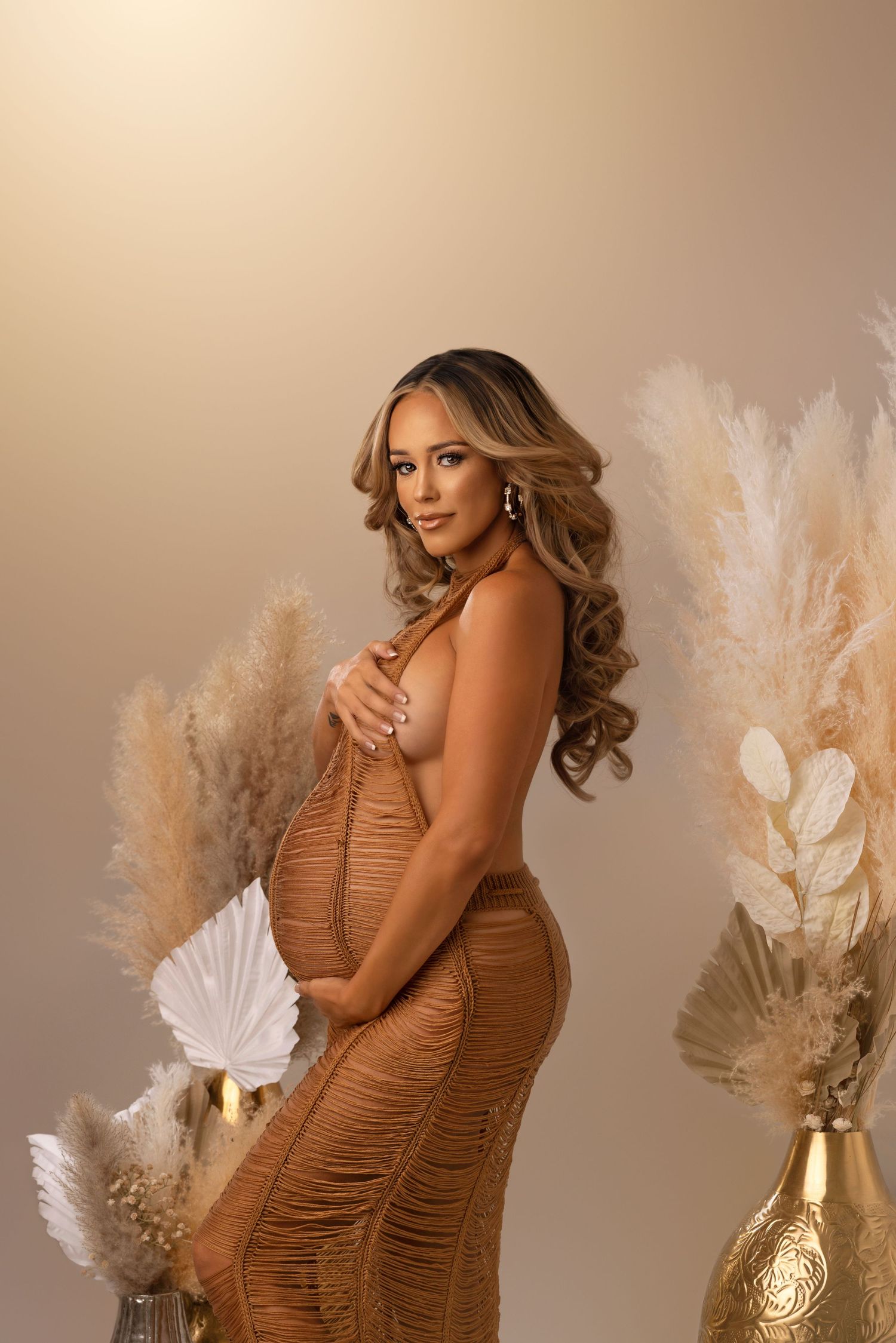 Elegant maternity portrait with brown ruched dress and pampas grass decor against neutral backdrop.
