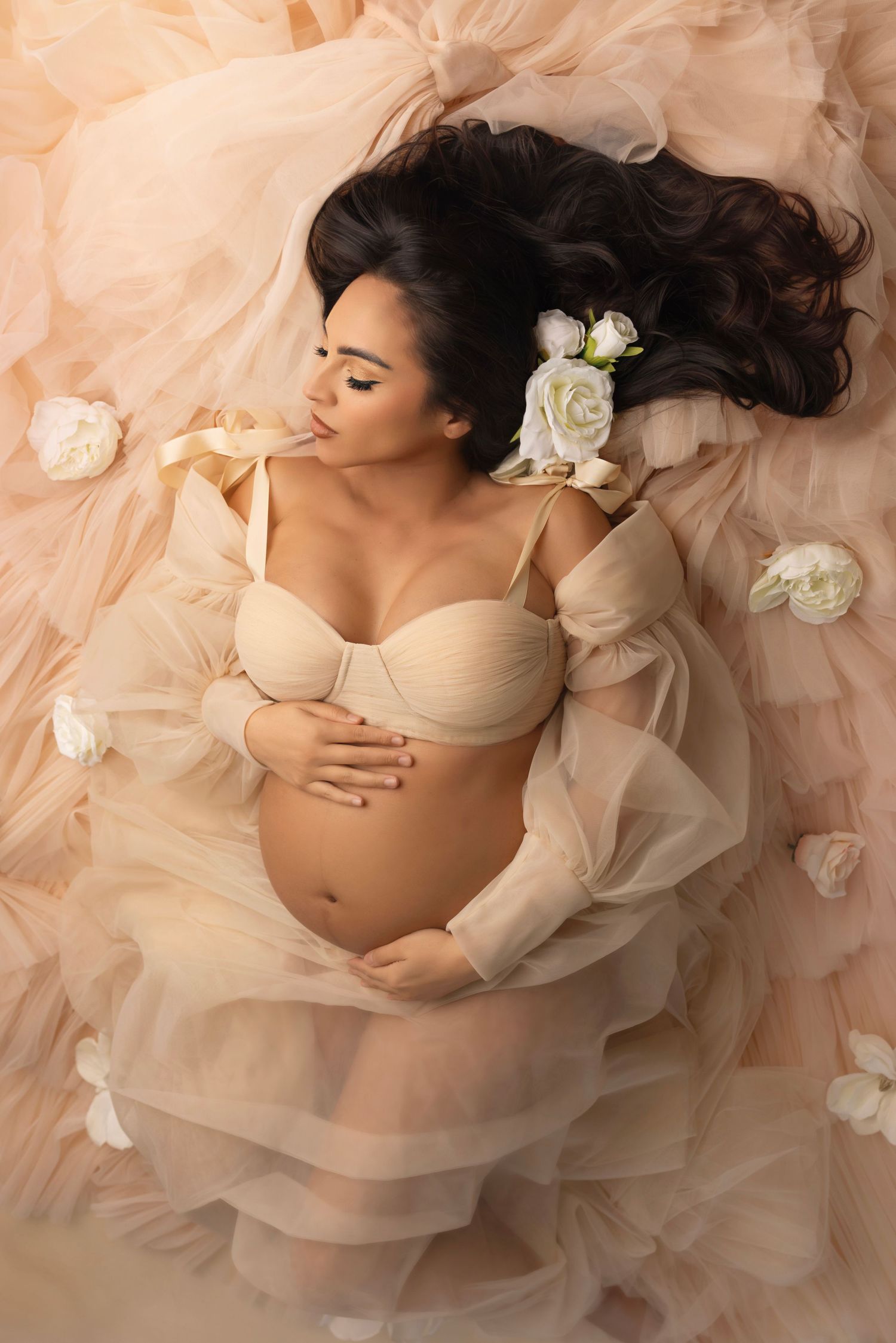 Ethereal maternity portrait with cream tulle layers and white floral accents.