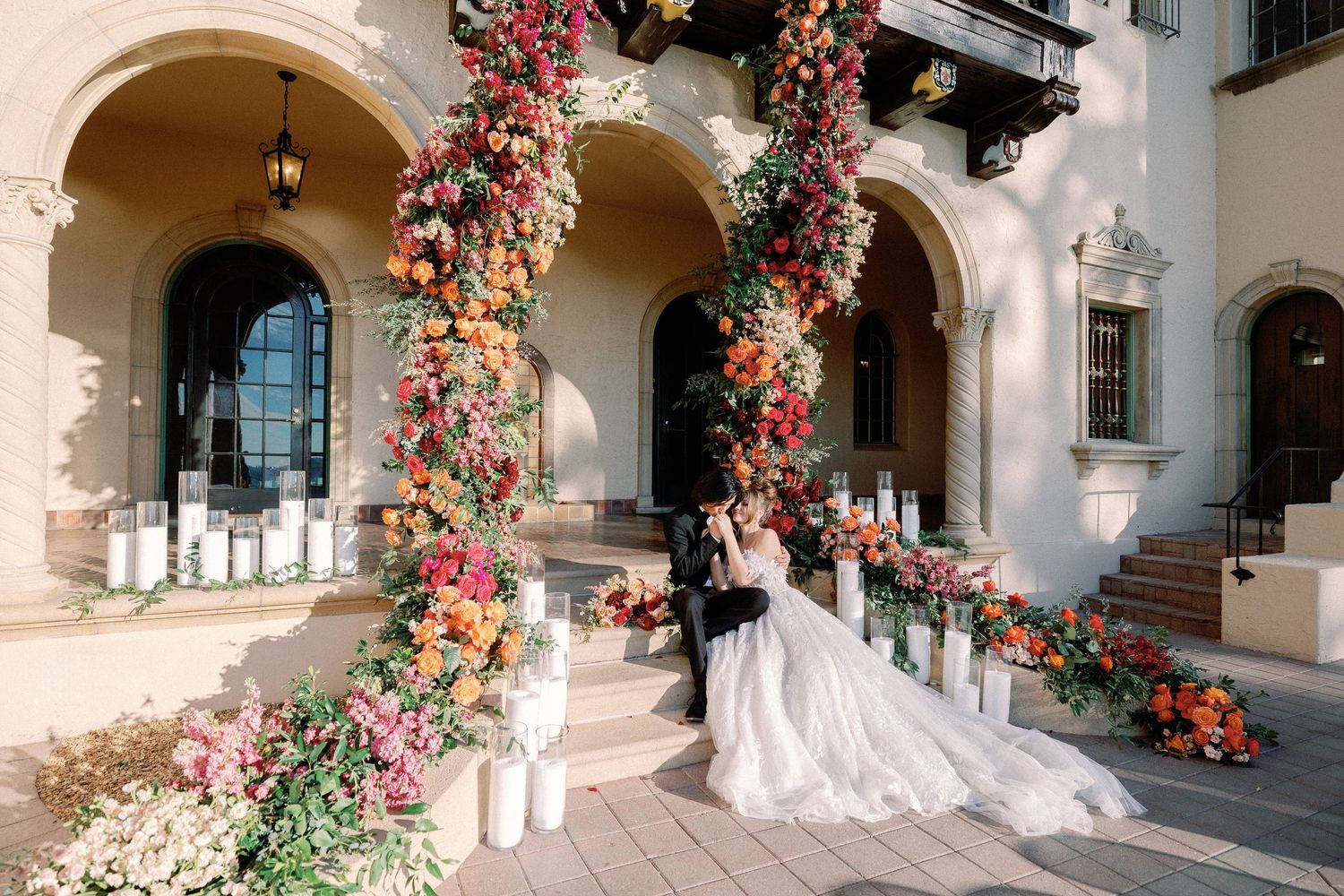 Romantic fine art wedding portrait of a bride and groom kissing on steps adorned with lush orange flowers and candles by KWON PHOTO.