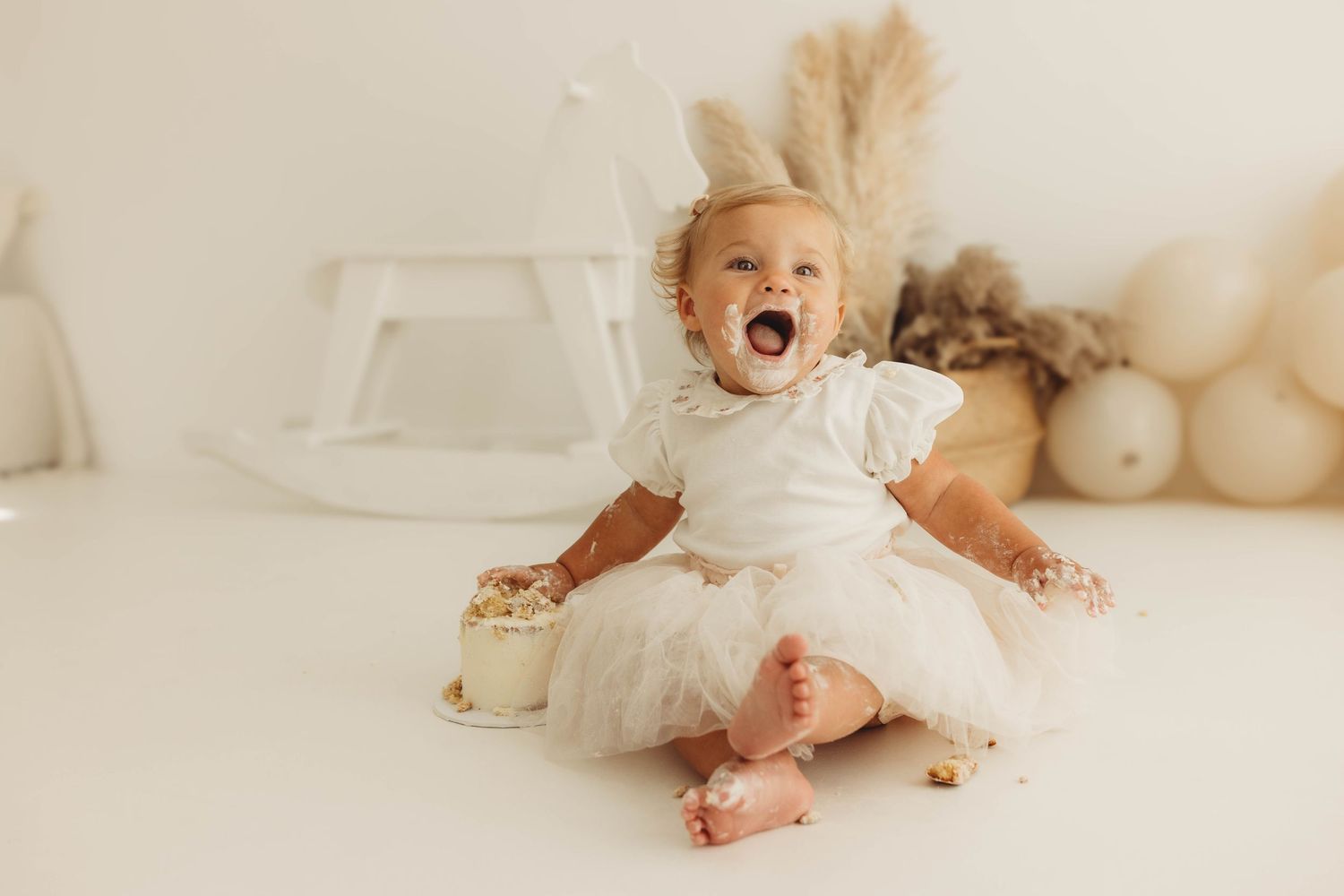 Two excited children in light colored outfits playing on white bedding.