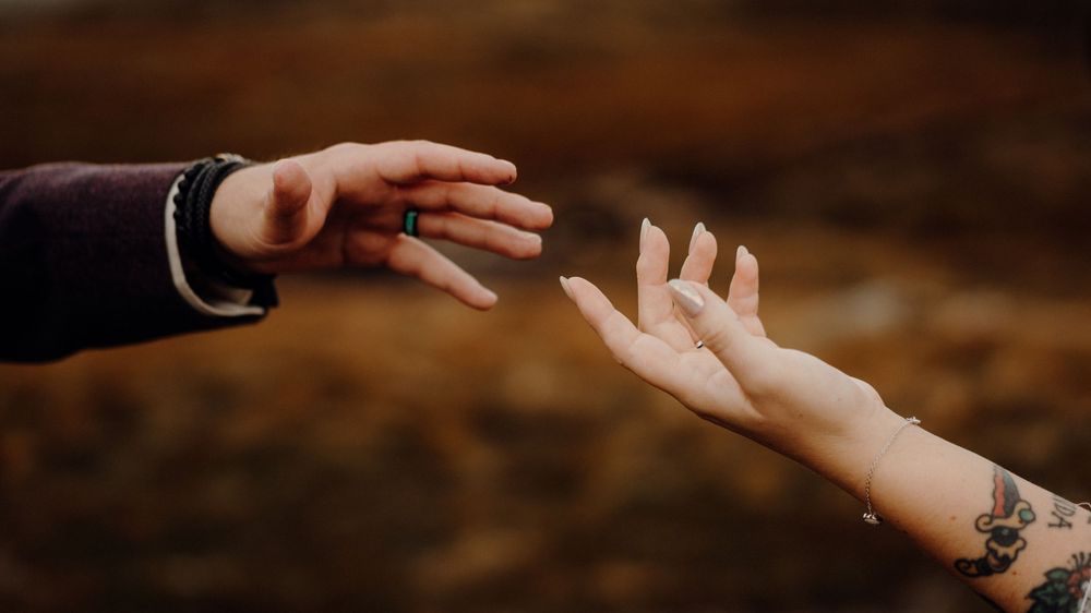 Two hands reach out to each other in a gentle touching gesture against a dark background.