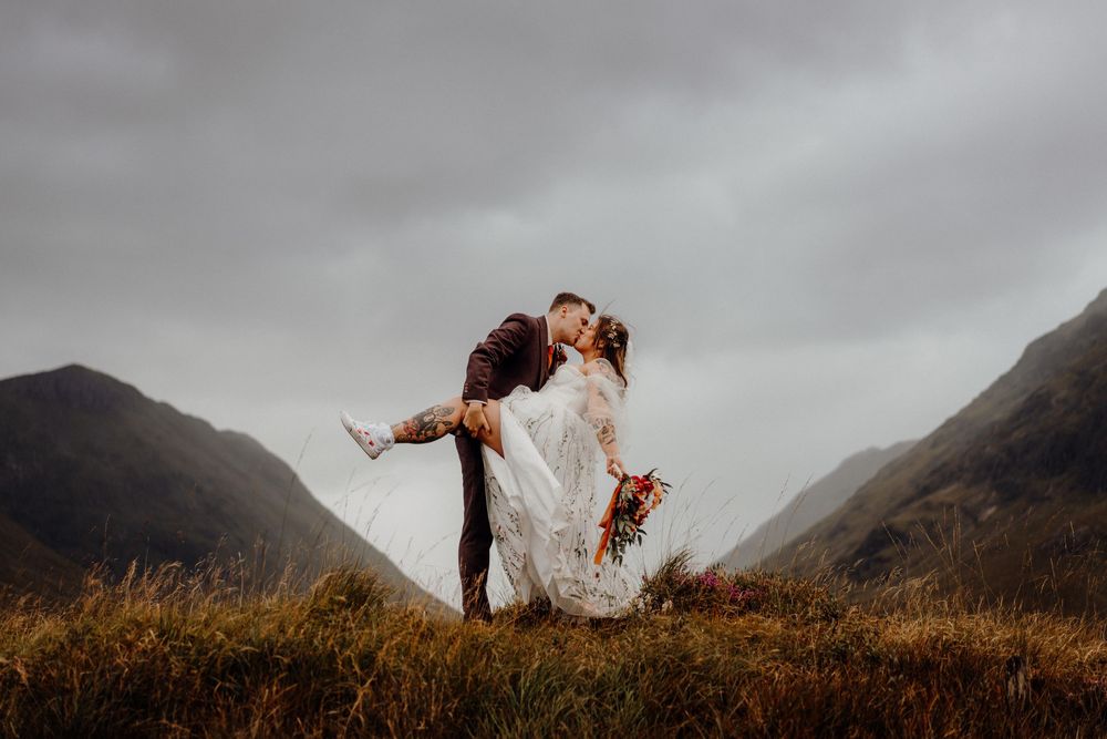 Dramatic panoramic mountain landscape under moody cloudy skies with golden grass in the foreground.