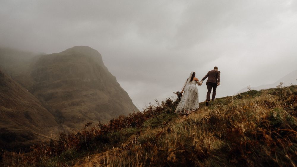 Silhouettes of figures standing on a hilltop against a cloudy mountain backdrop at dusk.