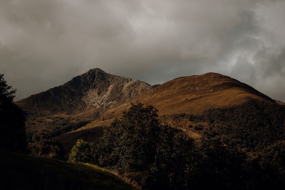 Dramatic mountain landscape with dark storm clouds gathering over rugged peaks and ridges at sunset.