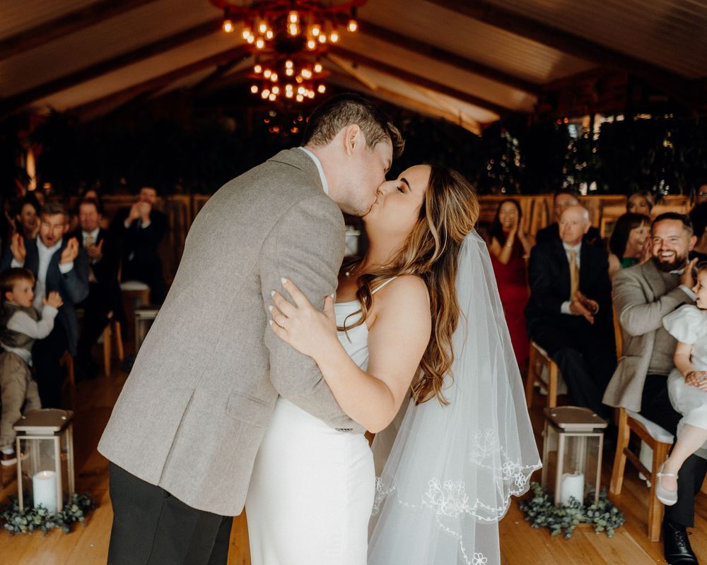 A couple shares their first dance as newlyweds on a wooden dance floor at an indoor wedding reception.