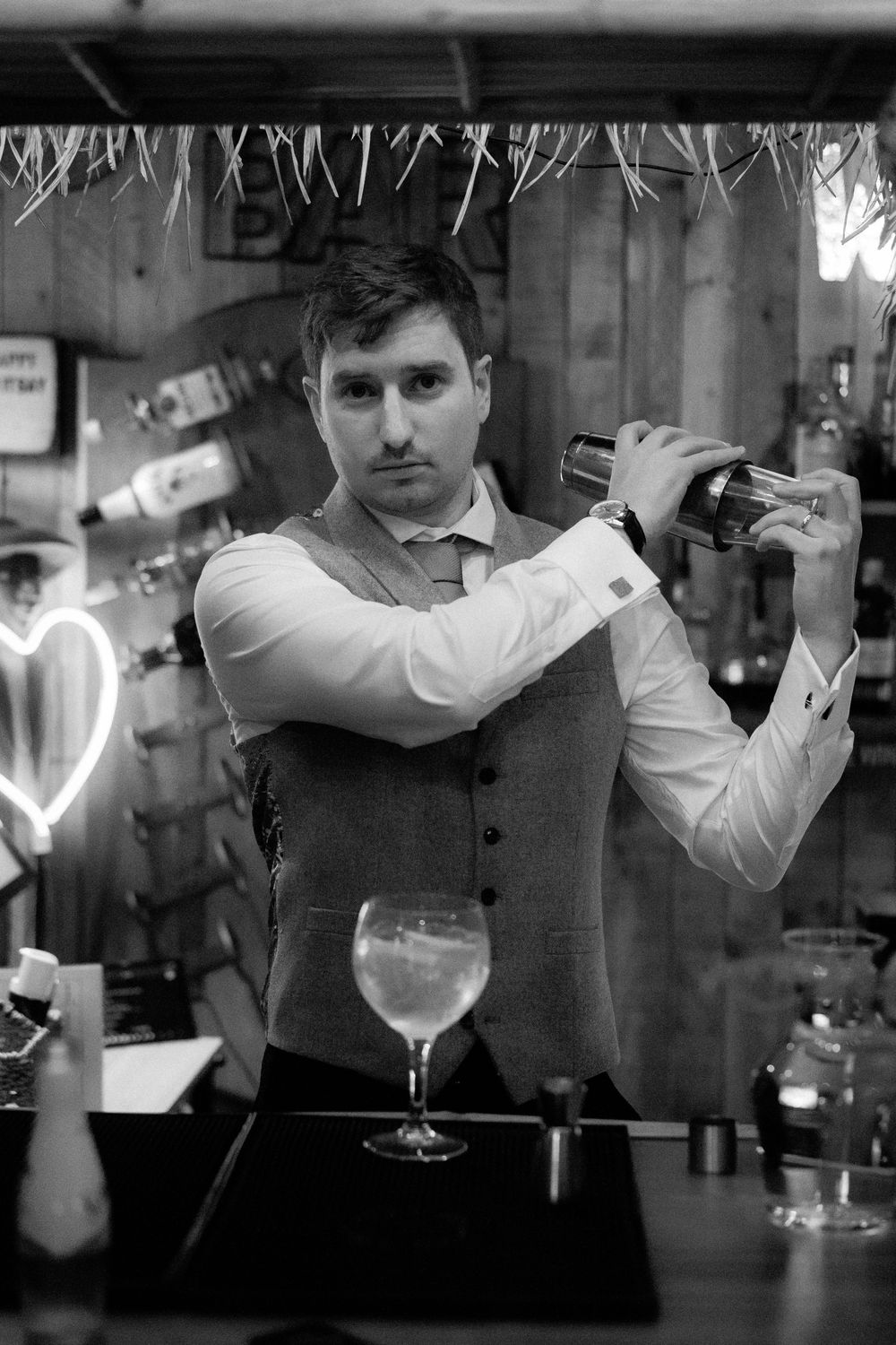 A black and white photo sequence shows a bartender preparing and pouring cocktails behind a bar counter.