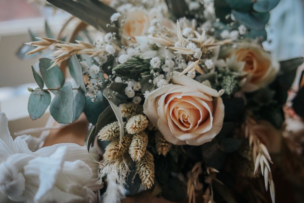 Elegant wedding bouquet featuring peach roses, eucalyptus leaves, and dried botanical elements in a muted color palette.