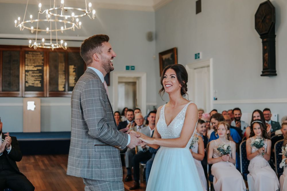 Joyful moment during wedding ceremony in an elegant hall with chandelier and wooden flooring.