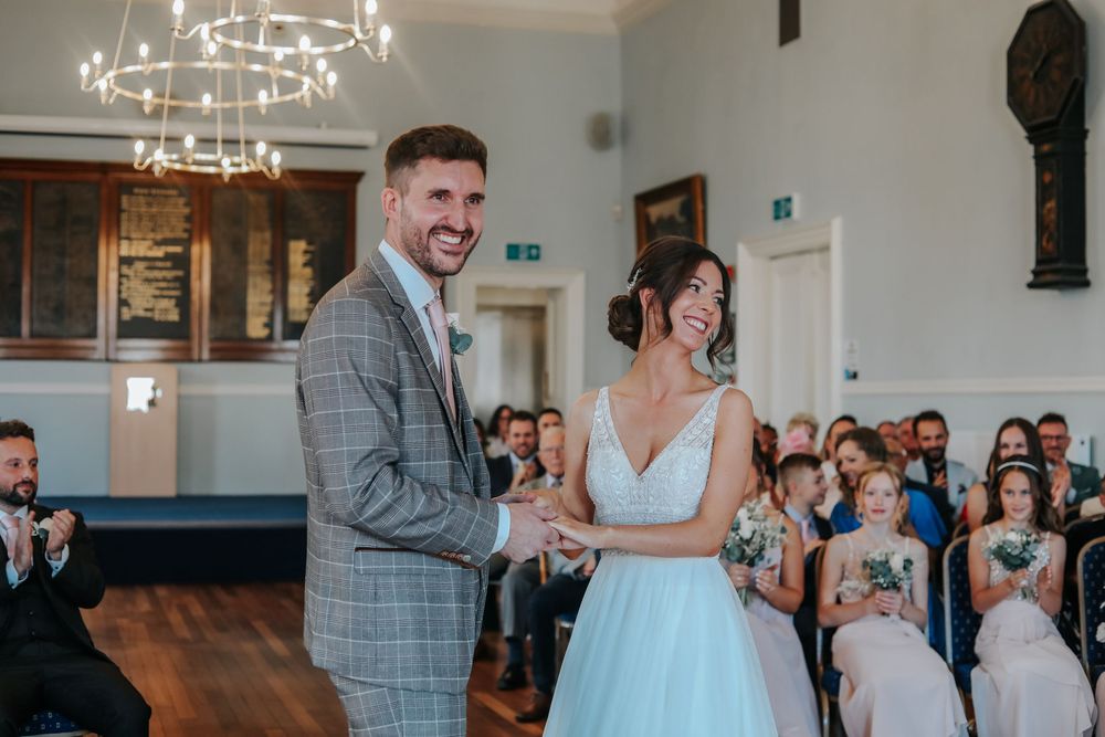 Candid moment of laughter shared during wedding ceremony under ornate chandelier.