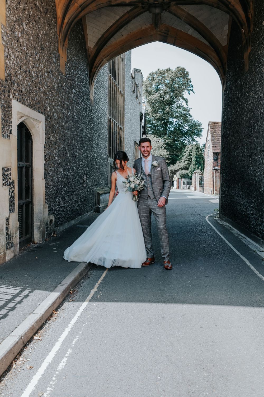 Couple walking through historic stone archway in wedding attire on their special day.