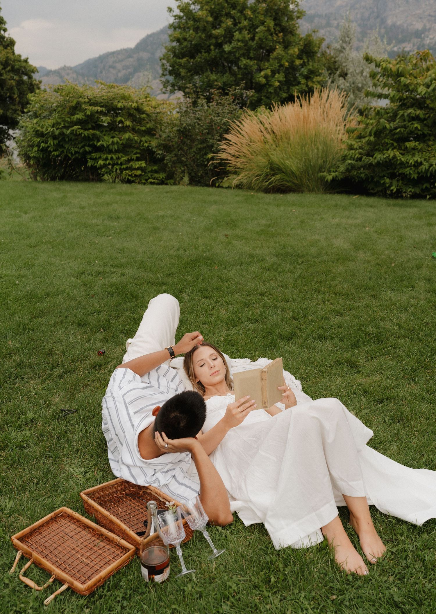 a picnic style okanagan engagement session on a summer day, while the woman reads a book, her groom to be stares at her lovingly.