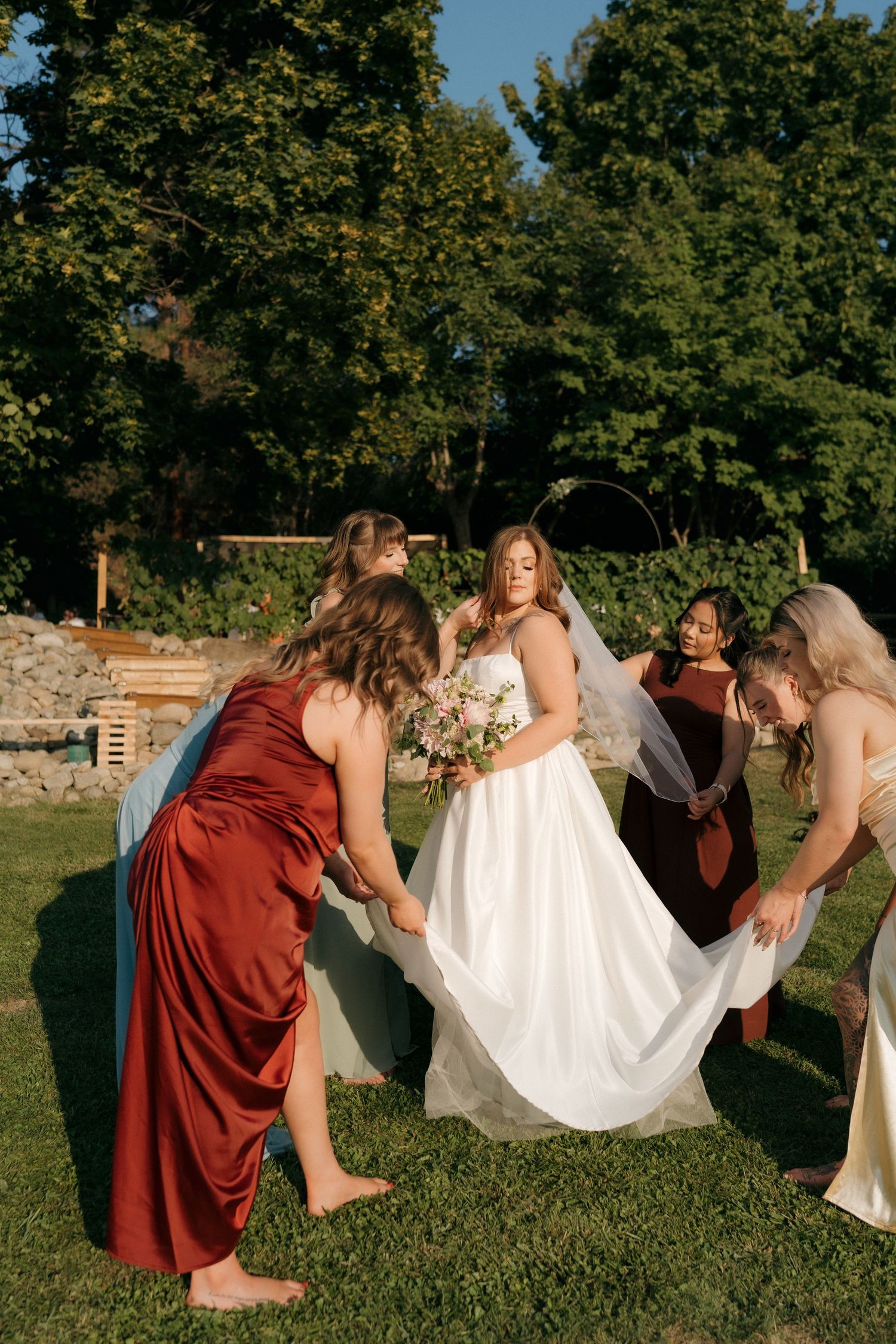 gorgeous okanagan bride glowing in the sunlight, her bridesmaids fix her stunning wedding gown