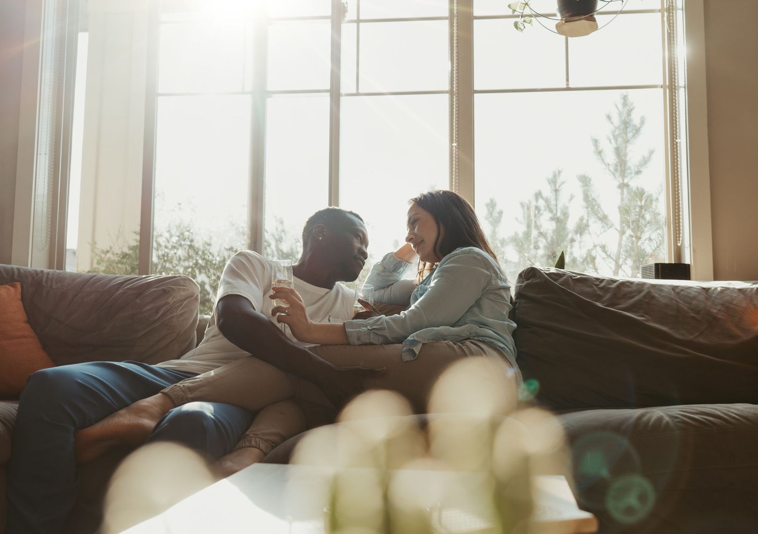 A biracial couple sitting closely on a cozy couch, wrapped in a warm embrace and gazing lovingly into each other's eyes in a softly lit room