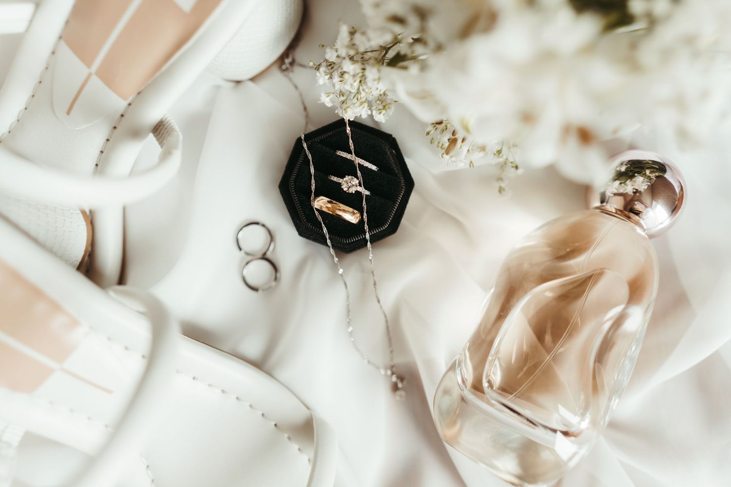 a beautiful detail shot photo of some engagement and wedding rings, placed carefully next to wedding shoes and perfume.