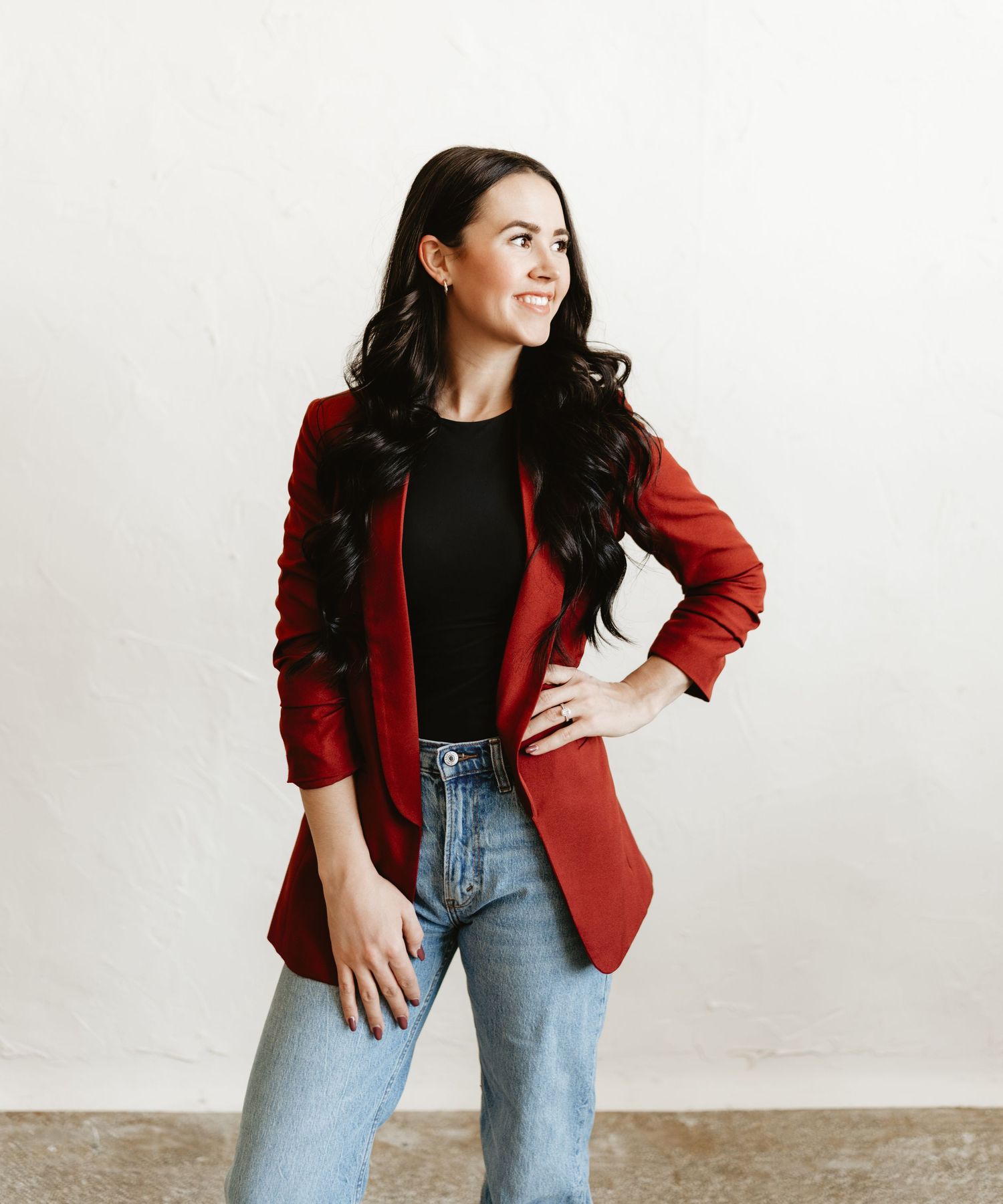 a professional business owner in a red tailored blazer, smiling confidently with her hand on her hip, against a neutral background.