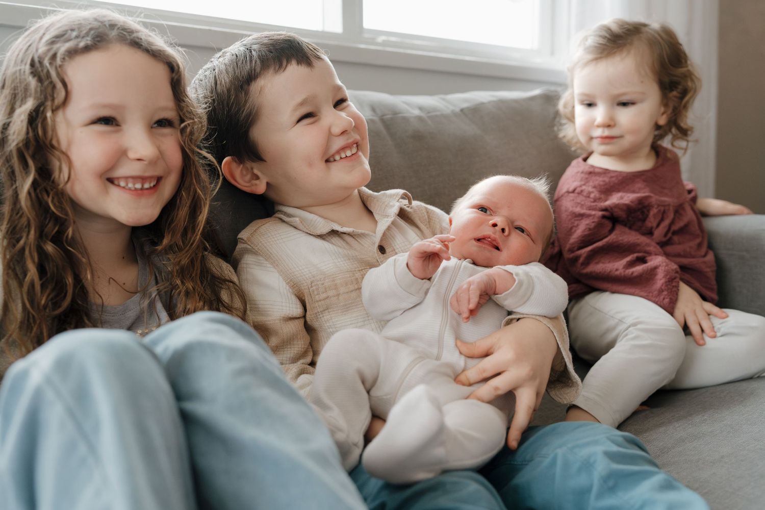 A newborn baby wrapped up in his smiling brother and sisters arms during a Summerland, BC in-home newborn session.