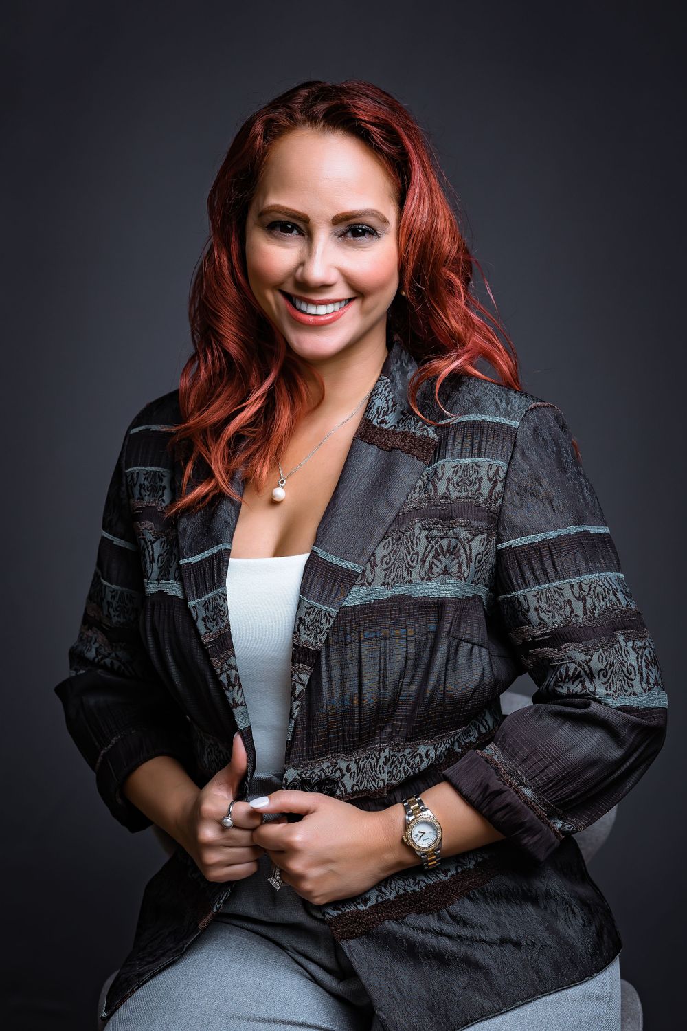 Portrait of person with red hair wearing patterned black blazer against dark background.