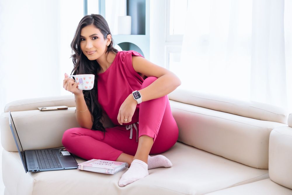 Person in pink loungewear working from home with laptop on couch.