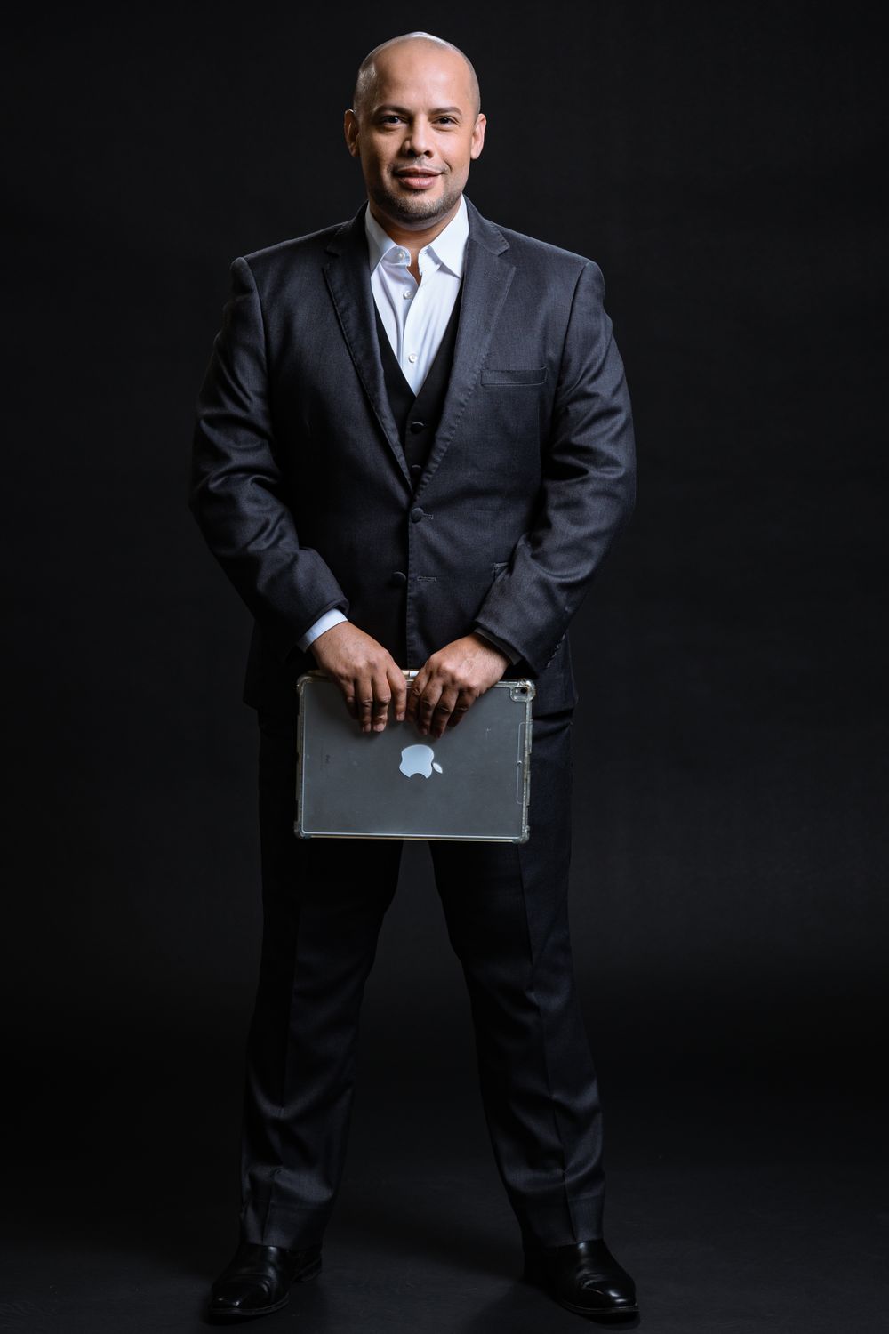 Professional holding laptop in business attire against dark backdrop.