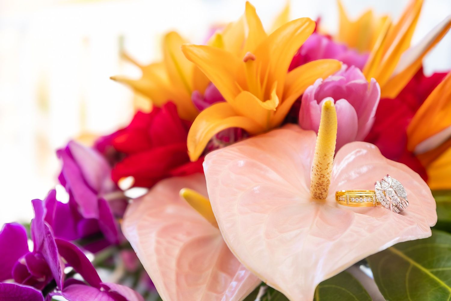Vibrant tropical wedding bouquet with orange lilies, pink anthuriums, and purple flowers adorned with a diamond engagement ring.