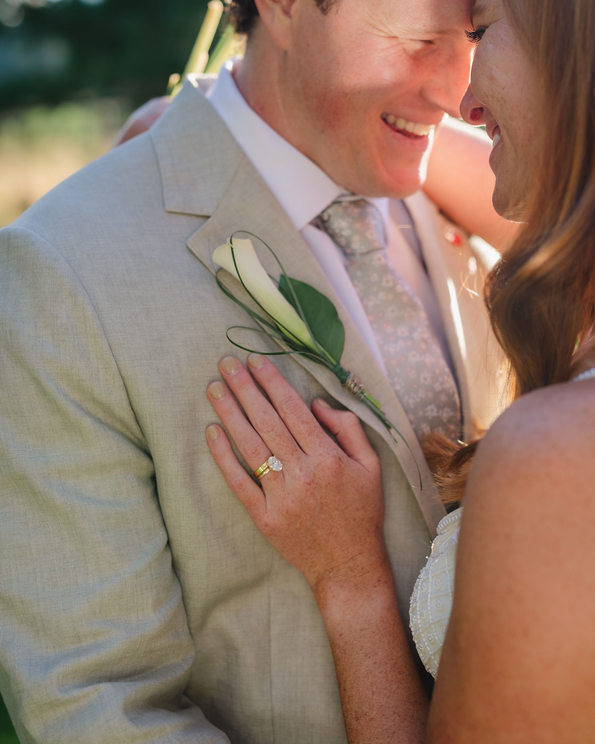A bride places her hand on the groom's gray suit lapel, showcasing her yellow diamond ring near a white calla lily boutonniere.