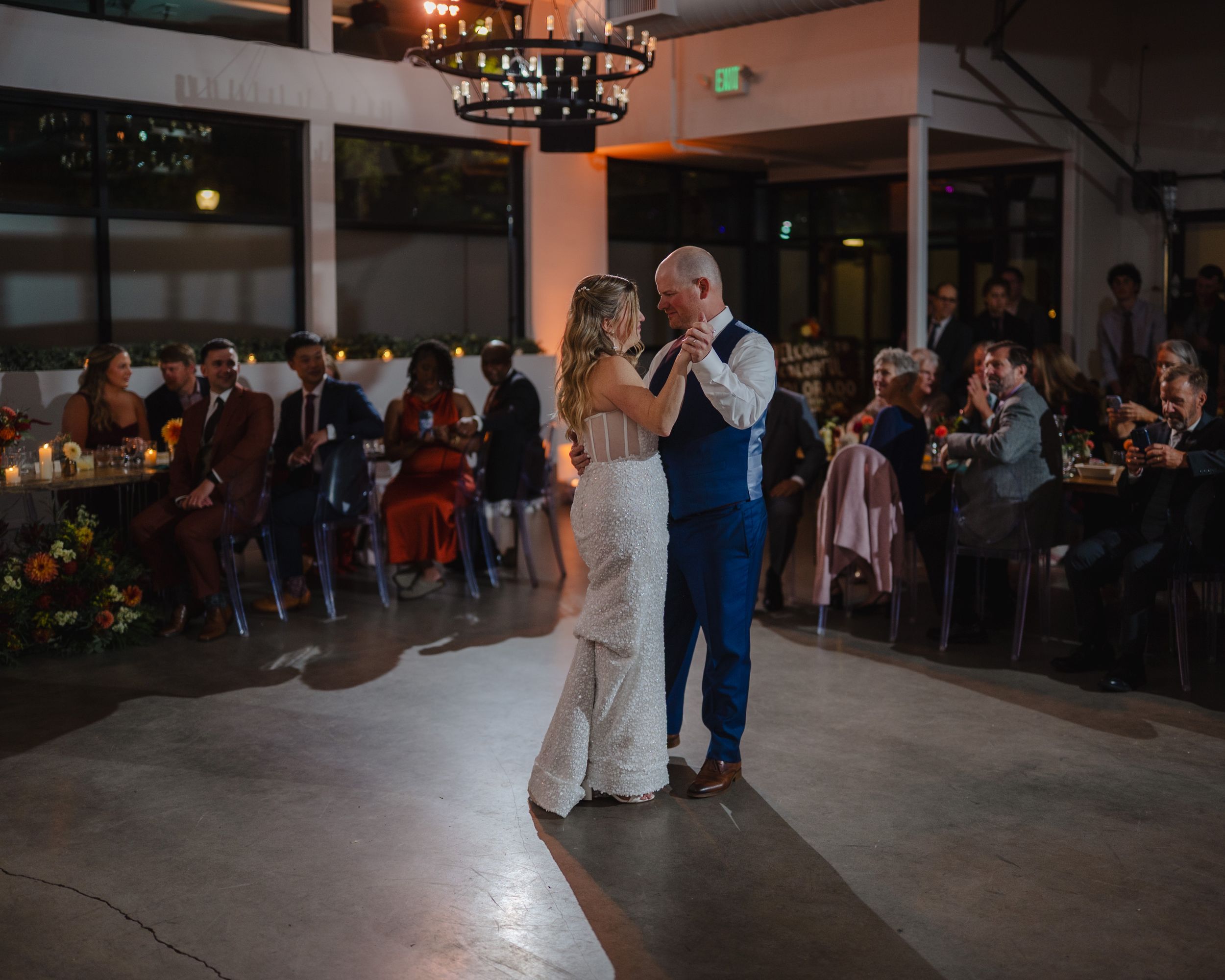 Couple sharing first dance at elegant wedding reception with guests watching in candlelit venue.