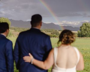 Bride and groom admire a stunning rainbow over mountain landscape at outdoor wedding.