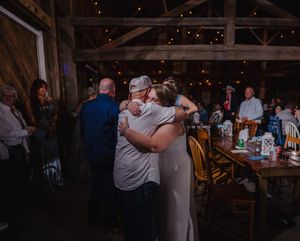 Guests sharing warm hugs at a rustic barn wedding reception with string lights and wooden decor.