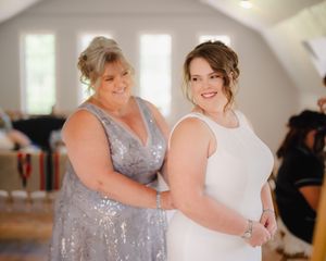 Mother helps bride with dress in bright white bridal suite before wedding ceremony.