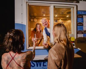 Couple serving ice cream from a food truck window to guests at a nighttime outdoor event.