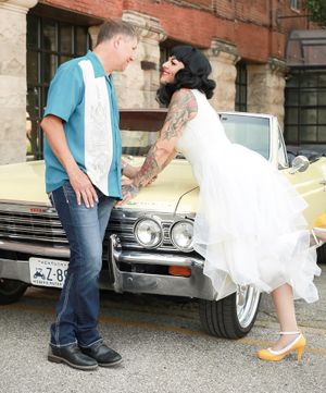 A couple in rockabilly style poses by a vintage yellow Chevrolet car during a retro-themed photo session.