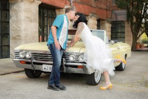 A couple poses playfully in front of a vintage yellow Cadillac with the bride wearing a short white dress and yellow shoes.