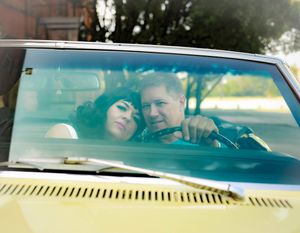 A romantic couple shares an intimate moment while sitting in a vintage car with yellow dashboard.