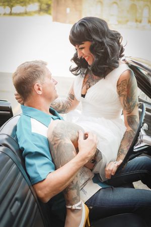 Intimate moment captured of a couple in classic car with woman in white dress showing off tattoo sleeves.