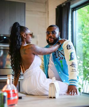 A romantic moment captured between two people in sunglasses, with her seated on a counter and him standing close.