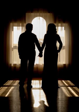 Silhouette of a couple holding hands while standing in front of a sunlit window.