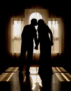 Silhouetted couple holding hands in an arch doorway with dramatic backlighting creating a romantic mood.