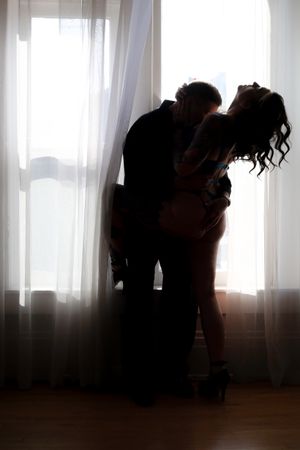 A silhouetted couple embracing in a romantic dance pose against a bright window with sheer curtains.